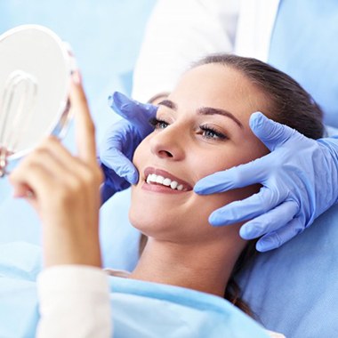 woman smiling in mirror after getting tooth-colored fillings in Avon, MA 