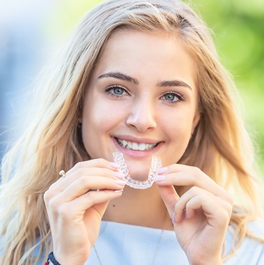Woman holding clear aligner from Invisalign in Avon