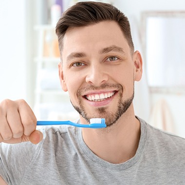 A man smiling and holding a toothbrush.